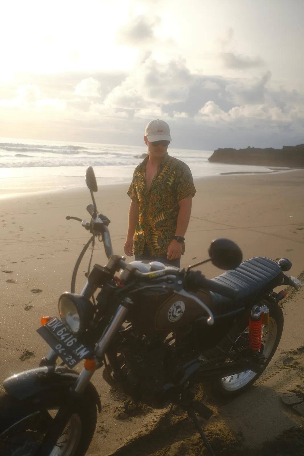 Dennis on the beach at sunrise next to a motorbike