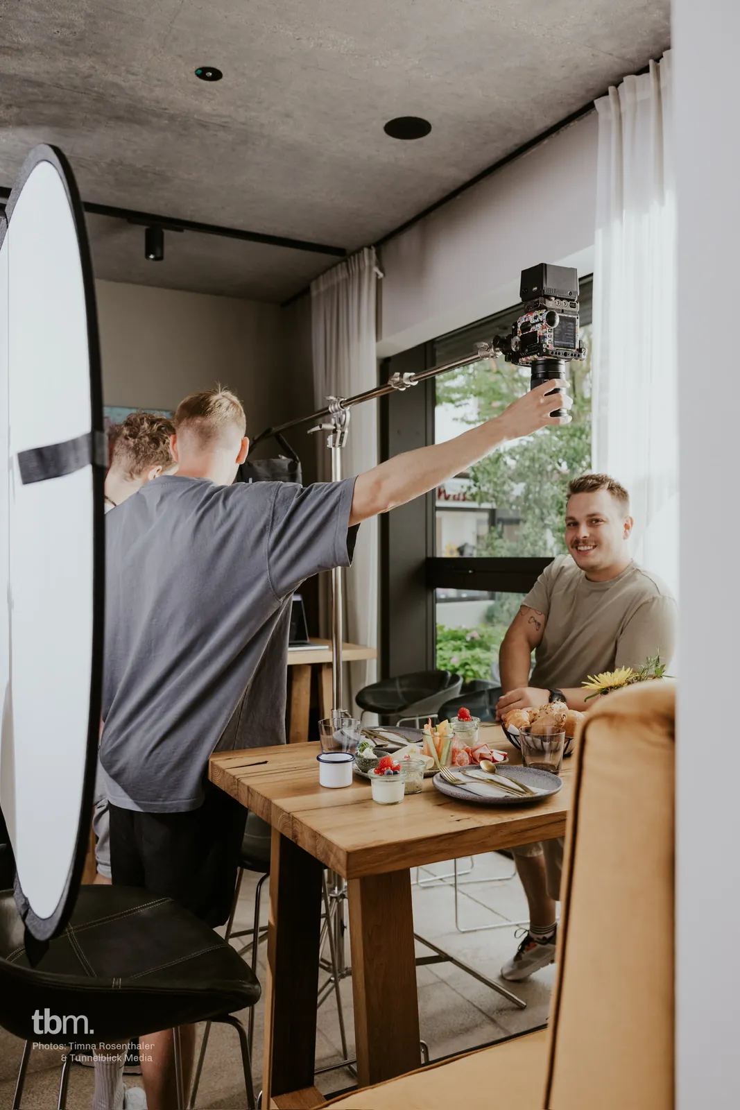 Breakfast-table shoot: a camera operator holds the camera on a pole, Dennis laughs into the lens