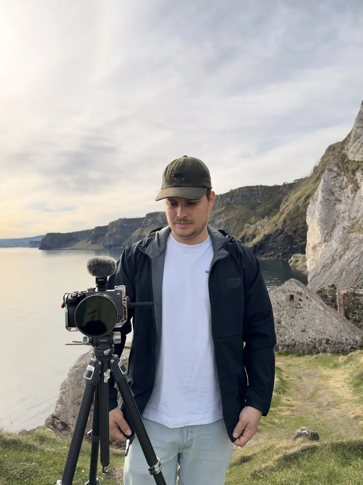 Dennis with a camera on a tripod on a cliff above the sea